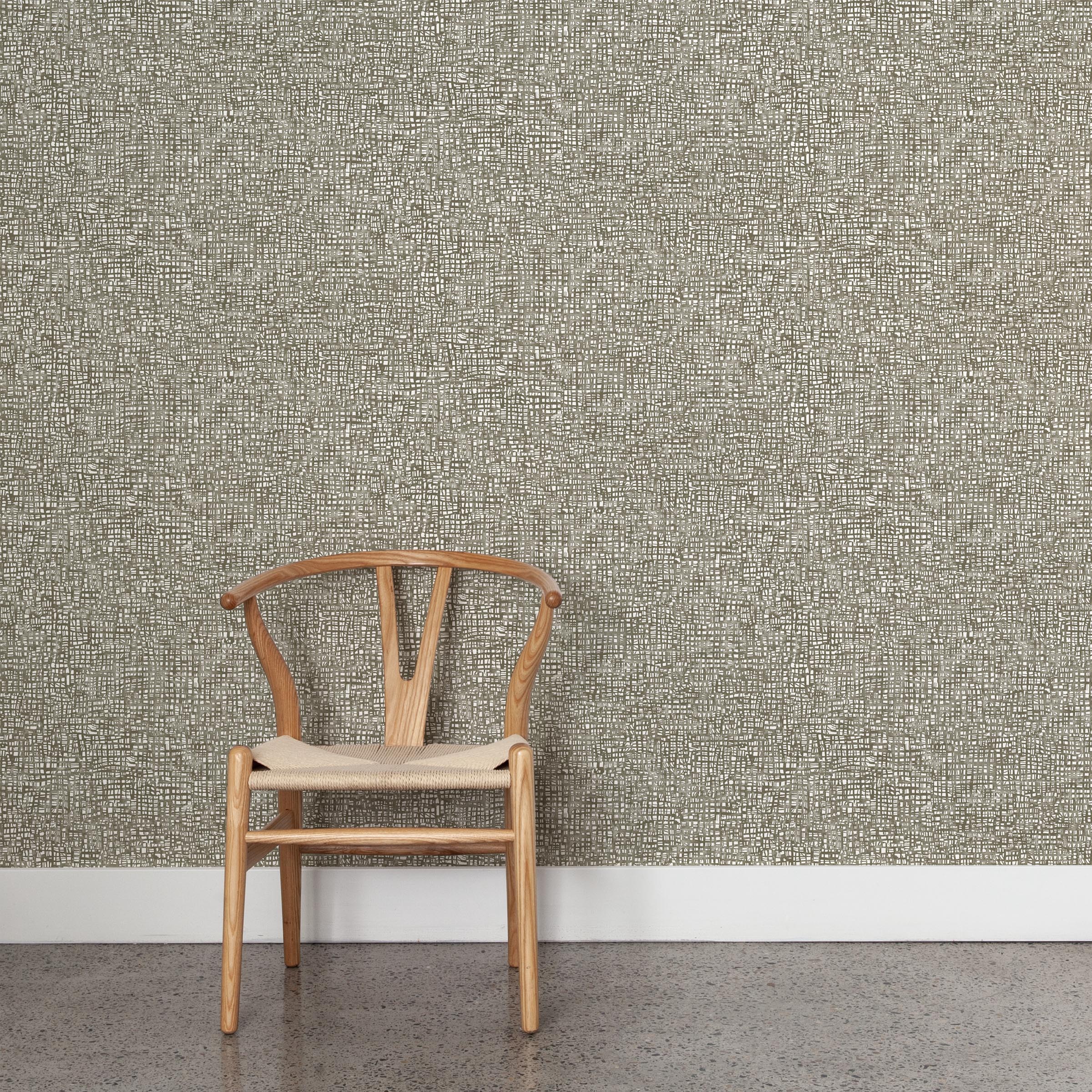 A wooden chair stands in front of a wall papered in a textural wicker pattern in mottled brown on a white field.