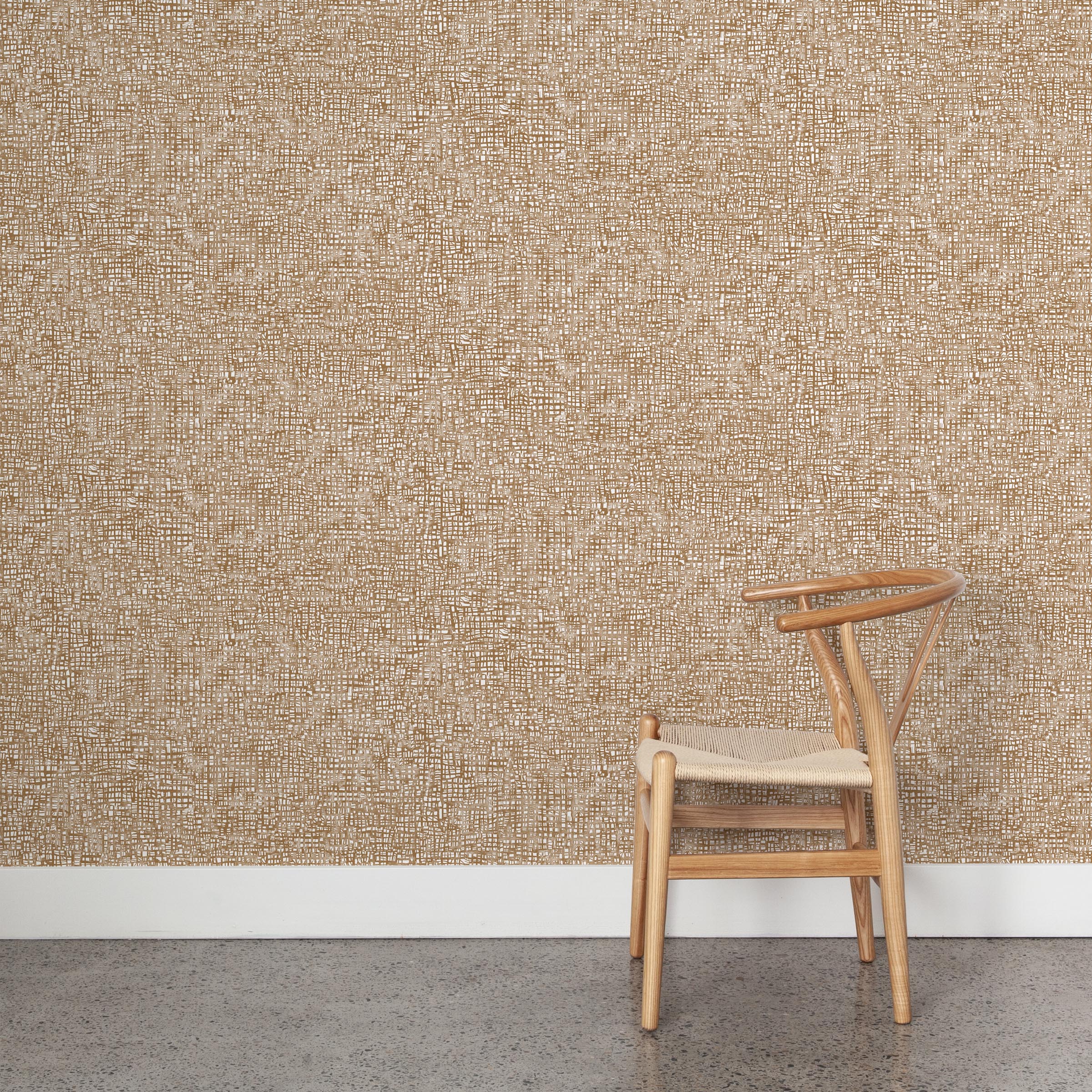 A wooden chair stands in front of a wall papered in a textural wicker pattern in mottled tan on a white field.