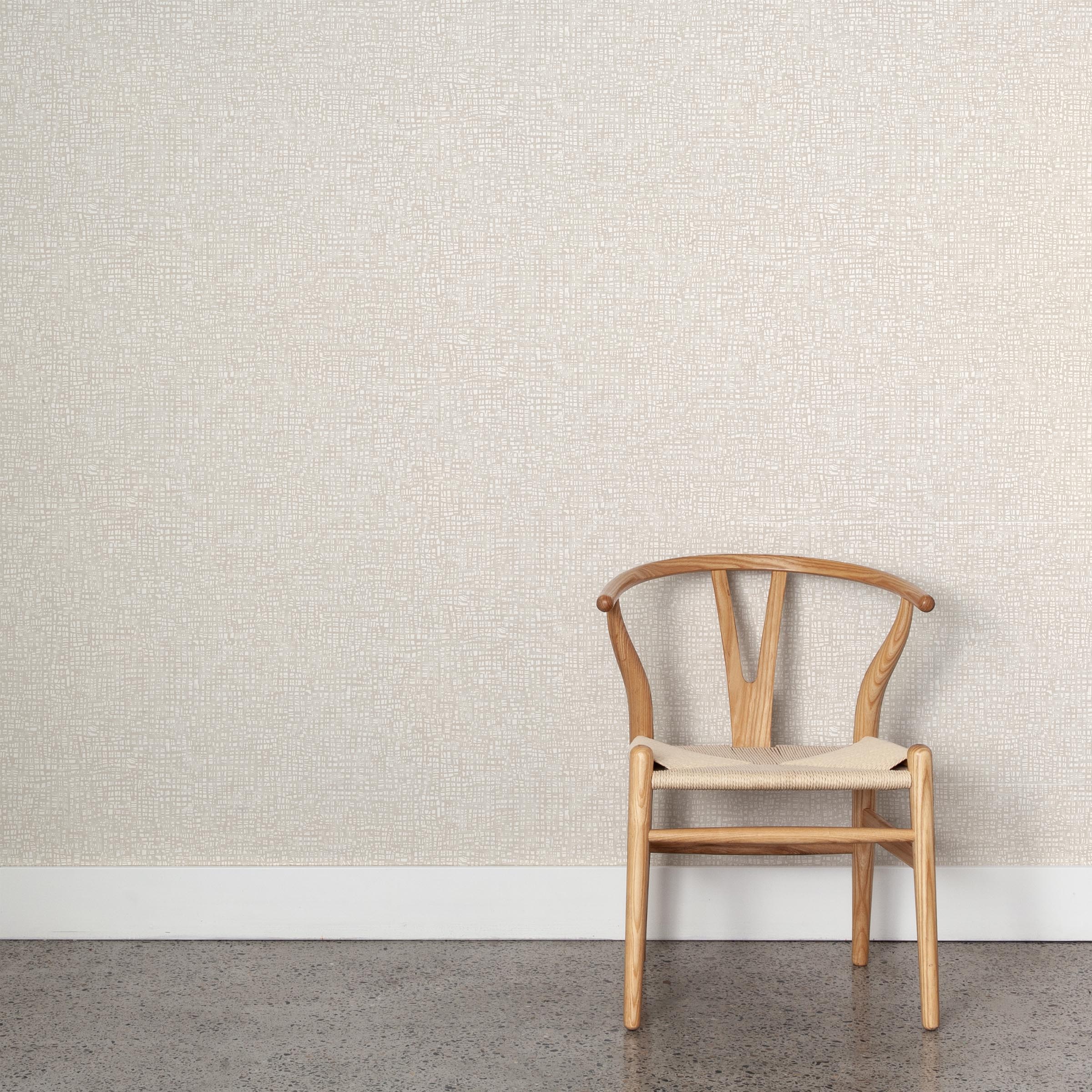 A wooden chair stands in front of a wall papered in a textural wicker pattern in mottled cream on a white field.