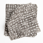 A stack of fabric swatches in a textural wicker pattern in mottled dark brown on a white field.