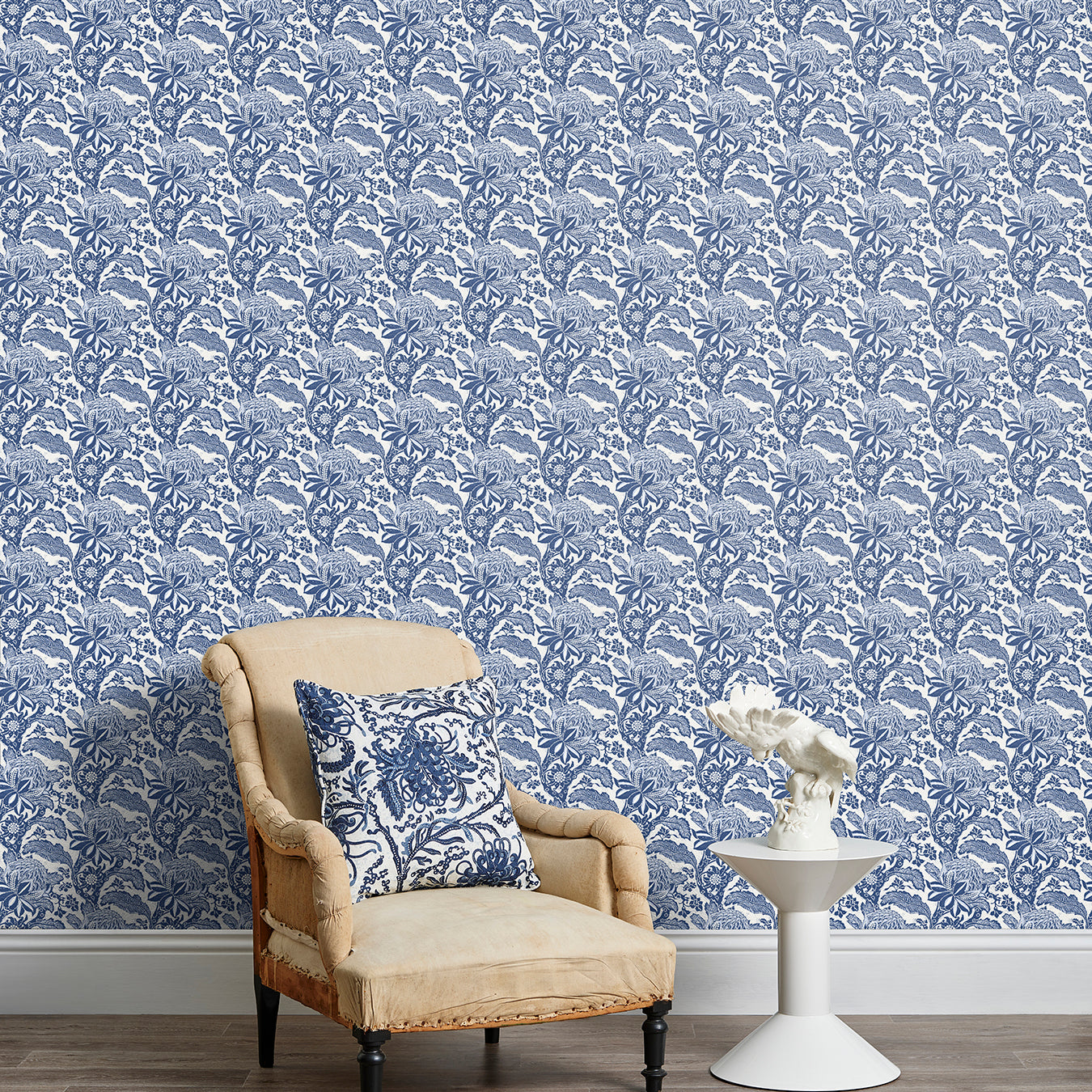 Armchair and end table in front of a wall papered in a repeating botanical print in navy and white.