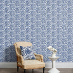 Armchair and end table in front of a wall papered in a repeating botanical print in navy and white.