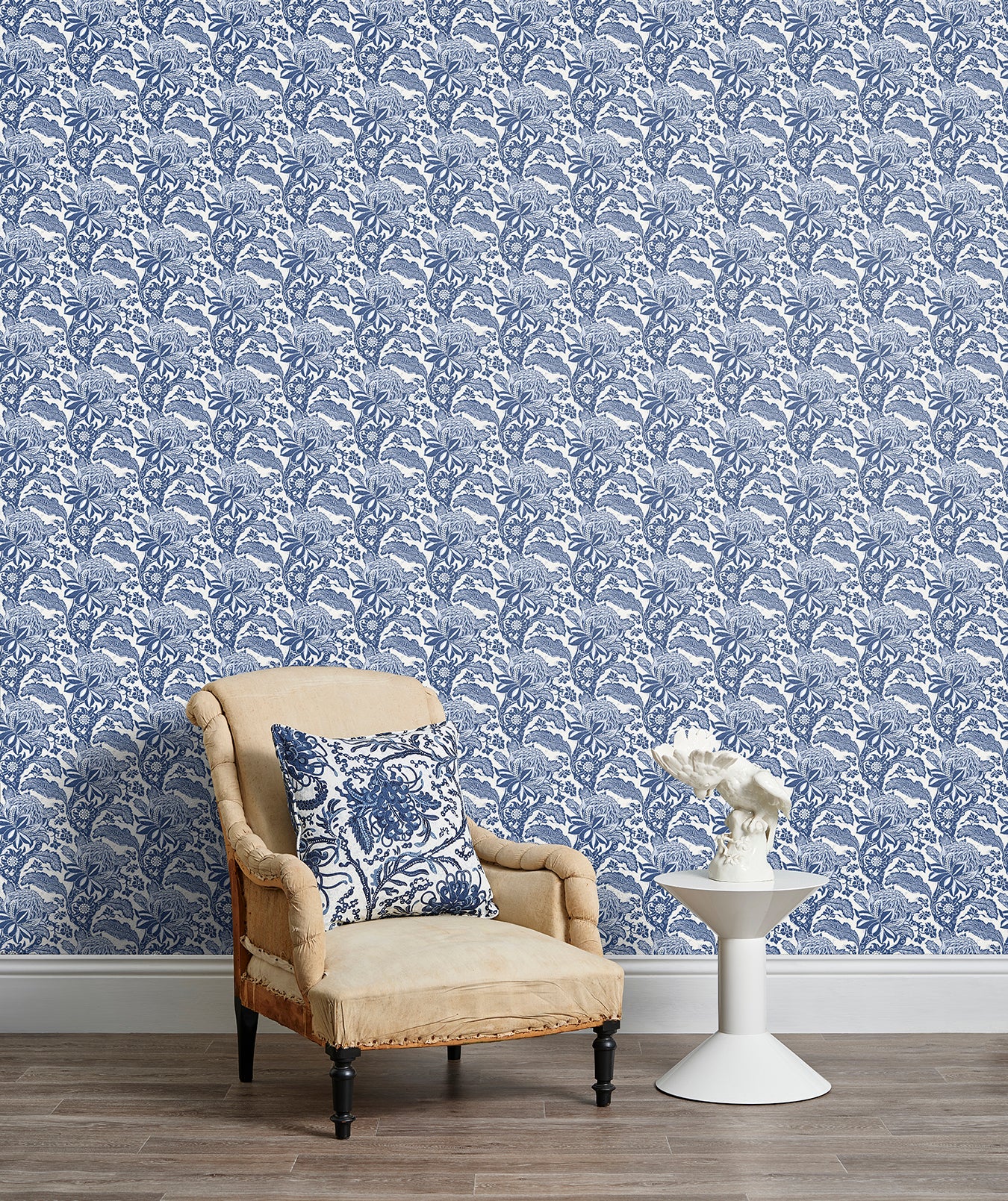 Armchair and end table in front of a wall papered in a repeating botanical print in navy and white.