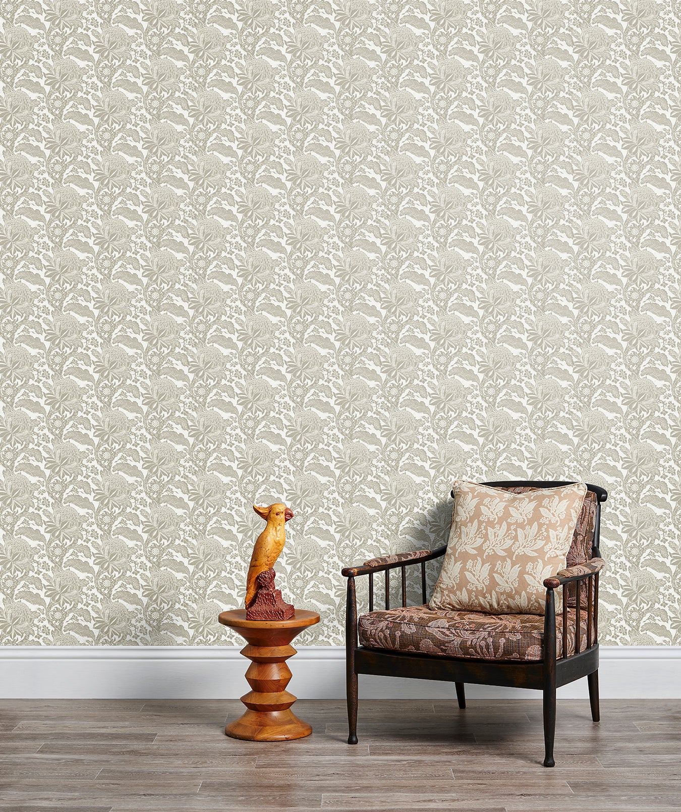 Armchair and end table in front of a wall papered in a repeating botanical print in cream and white.