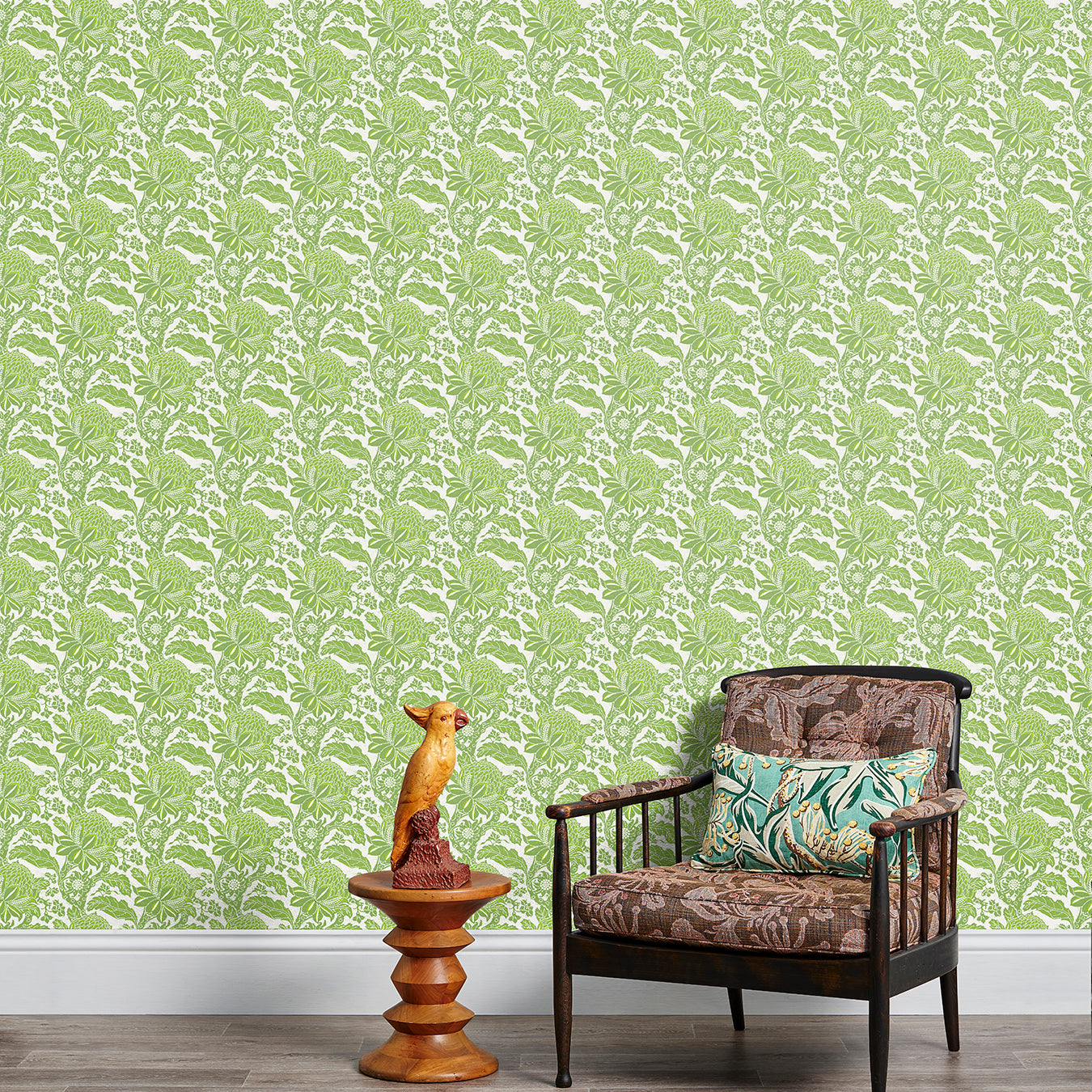 Armchair and end table in front of a wall papered in a repeating botanical print in green and white.