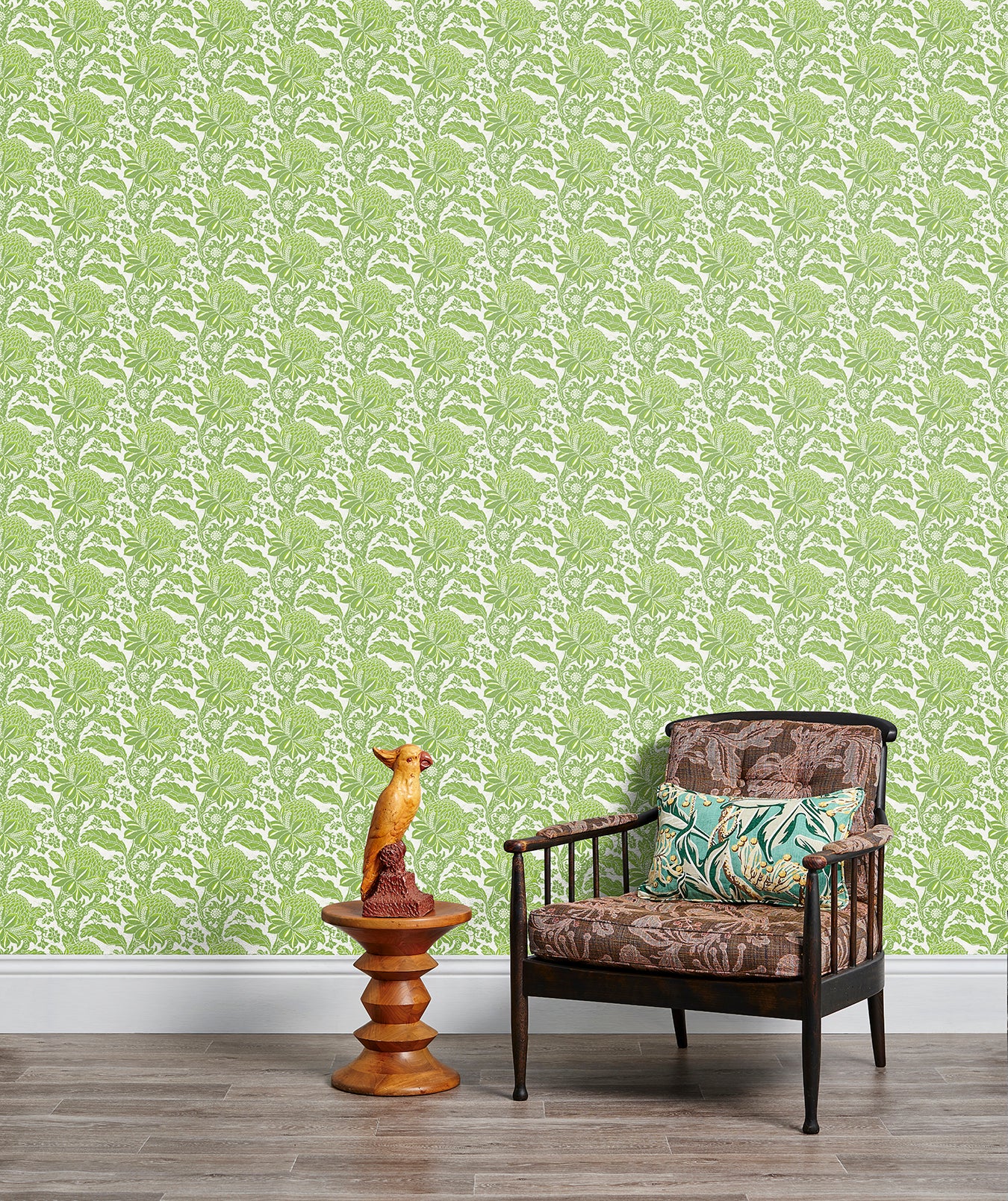 Armchair and end table in front of a wall papered in a repeating botanical print in green and white.