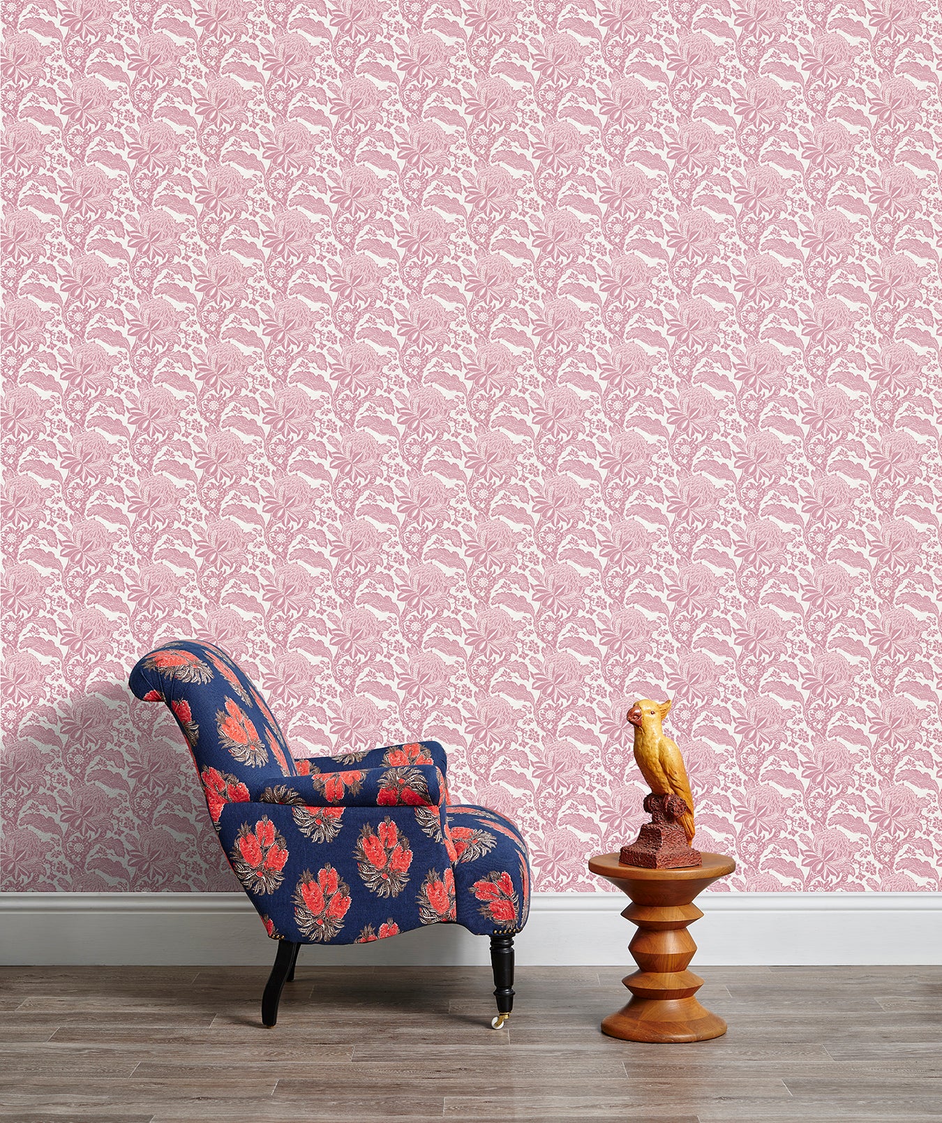 Armchair and end table in front of a wall papered in a repeating botanical print in pink and white.