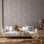 A livingroom furnished in neutral midcentury furniture with a wall papered in a playful animal print in white and gray.