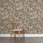 A wooden chair stands in front of a wall papered in an abstract leaf pattern in white on a brown watercolor field.