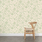 A wooden chair stands in front of a wall papered in a playful animal and tree print in green on a cream field.