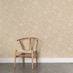 A wooden chair stands in front of a wall papered in a playful animal and tree print in white on a tan field.