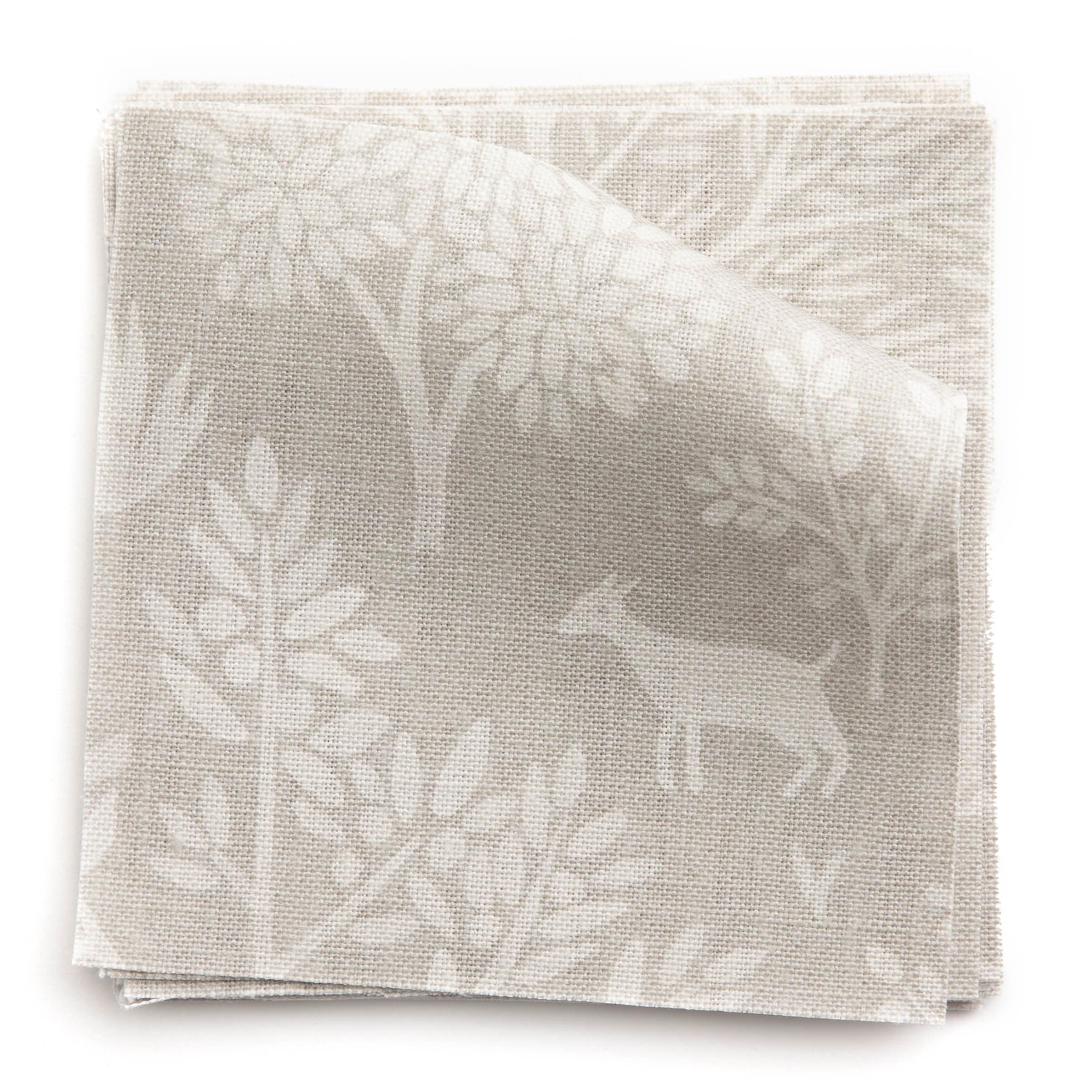 A stack of fabric swatches in a playful animal and tree print in white on a greige field.