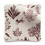 A stack of fabric swatches in a playful animal and tree print in purple on a greige field.