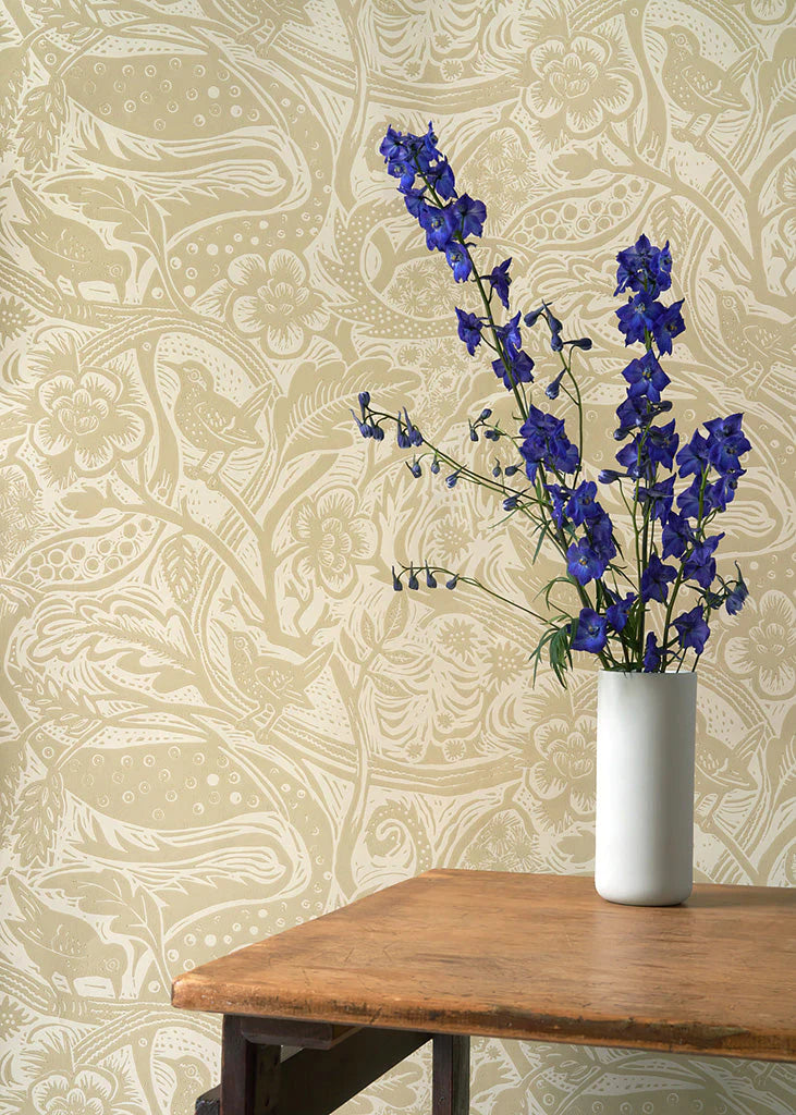 A vase of flowers stands in front of a wall papered in a playful wren and flower print in tan and cream.