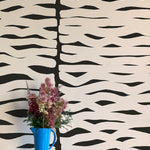 A vase of flowers stands in front of a wall papered in an abstract zigzag pattern in cream on a black field.