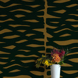 A vase of flowers stands in front of a wall papered in an abstract zigzag pattern in black on a brown field.