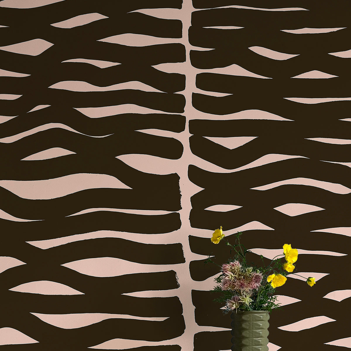 A vase of flowers stands in front of a wall papered in an abstract zigzag pattern in black on a light pink field.