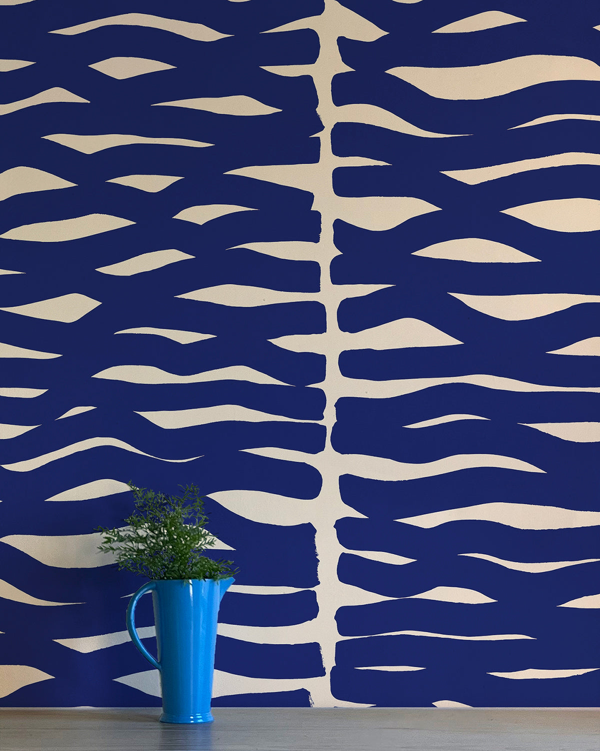 A vase of flowers stands in front of a wall papered in an abstract zigzag pattern in navy on a tan field.