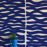 A vase of flowers stands in front of a wall papered in an abstract zigzag pattern in navy on a tan field.