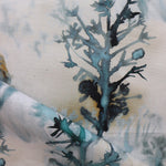 Detail of draped fabric yardage in an abstract botanical print in shades of turquoise, gray and gold on a cream field.