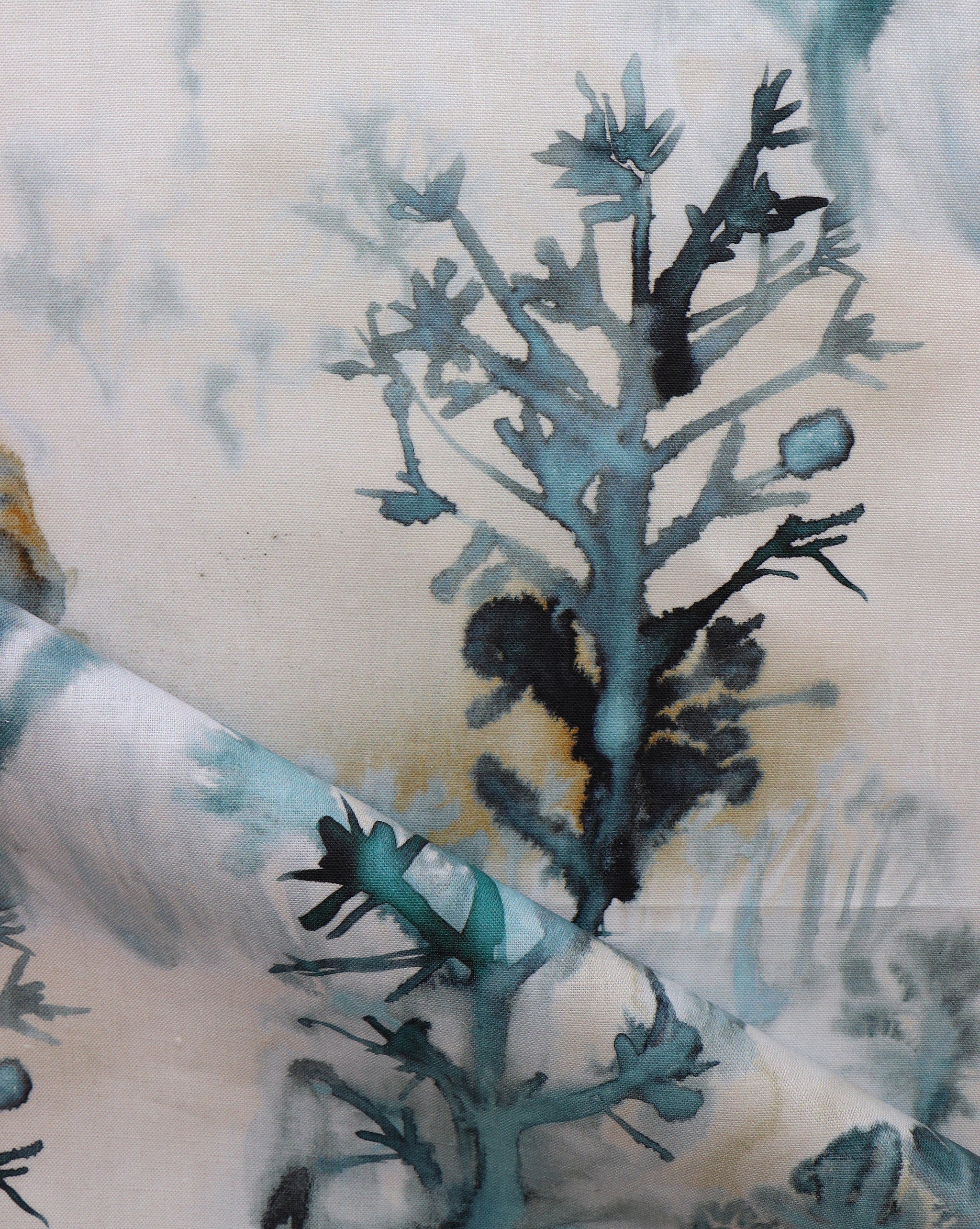 Detail of draped fabric yardage in an abstract botanical print in shades of turquoise, gray and gold on a cream field.