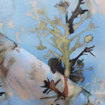 Detail of draped fabric yardage in a watercolor tree print in shades of tan and gray on a blue field.