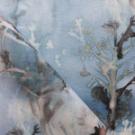 Detail of draped fabric yardage in an abstract botanical print in shades of gray and turquoise on a blue field.