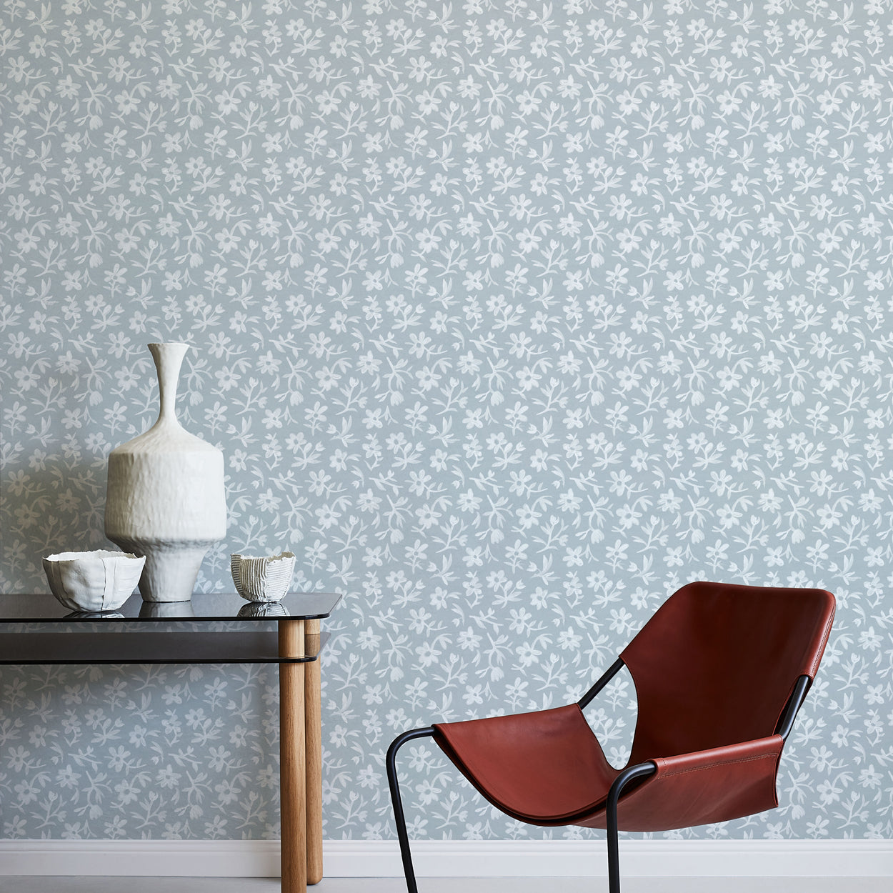 Modern brown chair and small table against a light blue floral wallpapered wall.