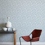 Modern brown chair and small table against a light blue floral wallpapered wall.