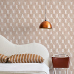 A modernist bed, hanging lamp and chair stand in front of a wall papered in an abstract scalloped print in tan and cream.