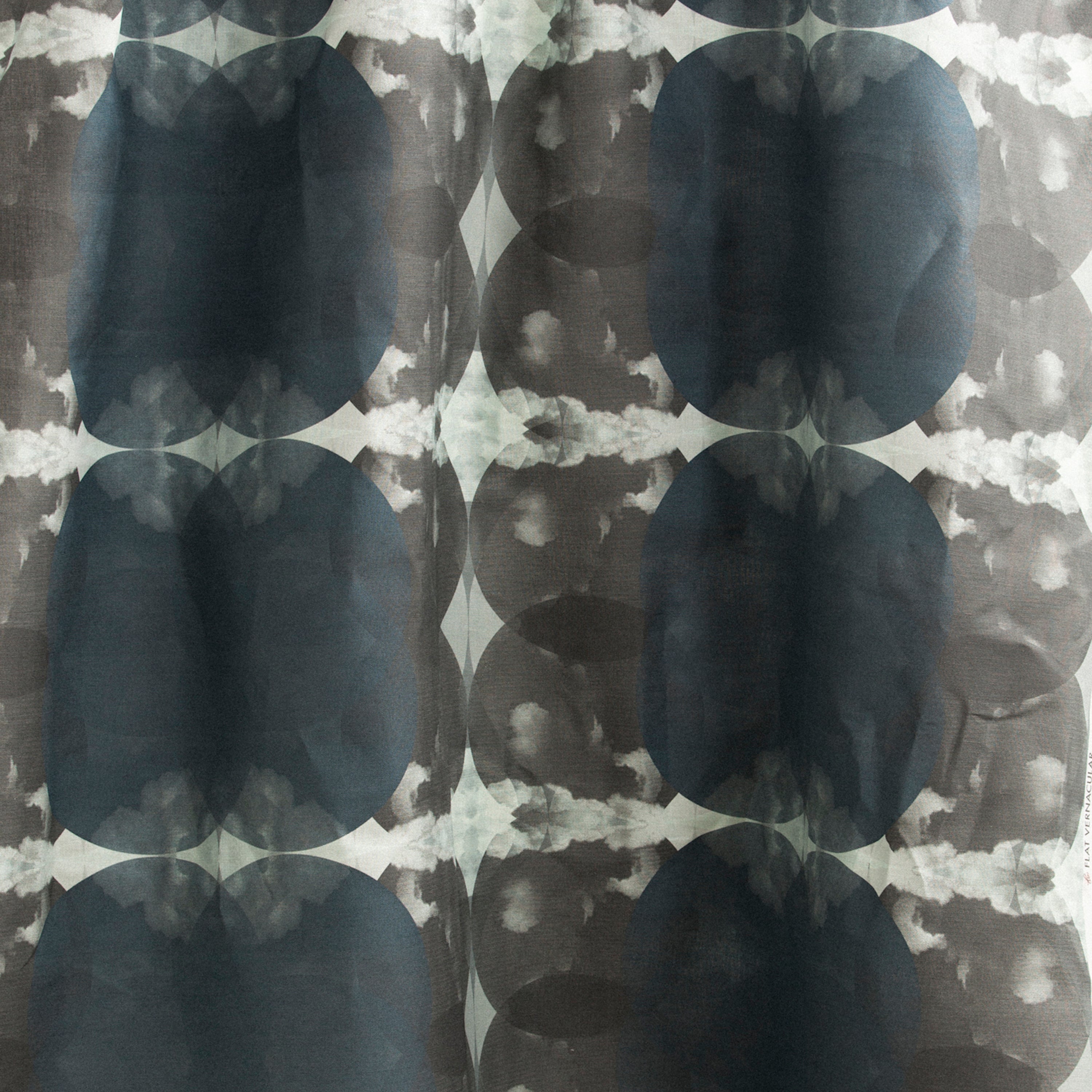 Draped fabric yardage in a cloudy ink blot print in shades of gray and blue on a light gray field.