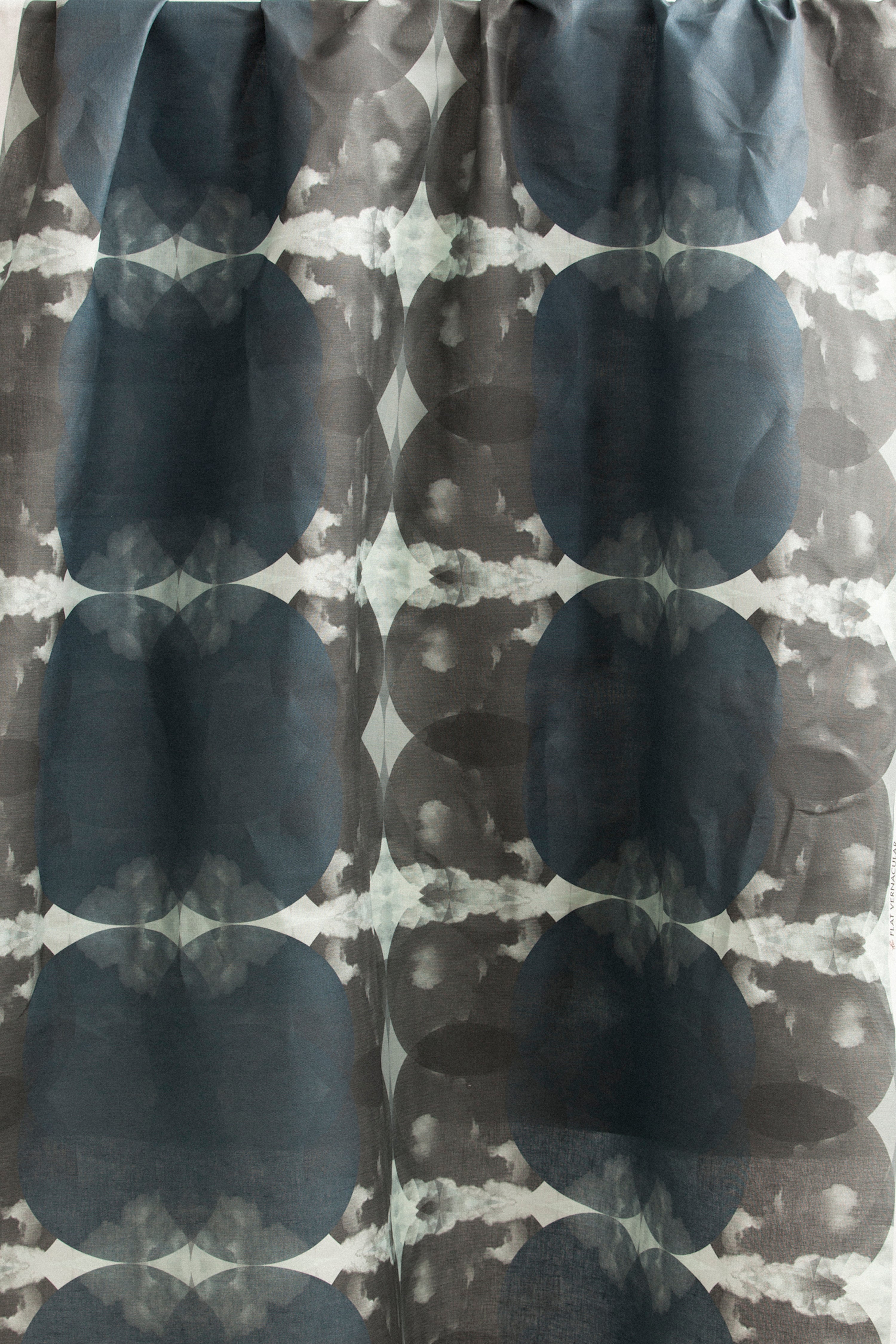 Draped fabric yardage in a cloudy ink blot print in shades of gray and blue on a light gray field.