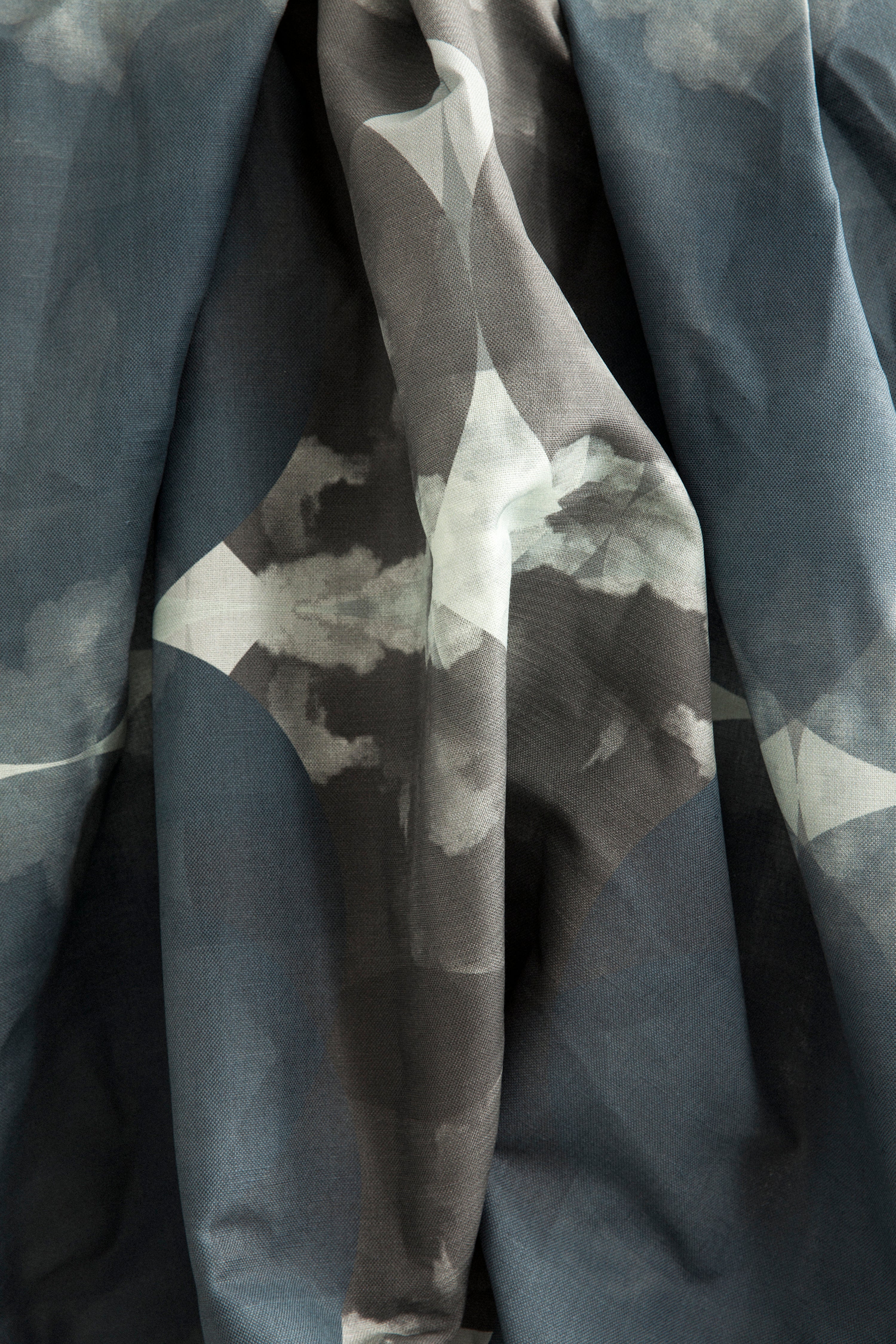 Crumpled fabric yardage in a cloudy ink blot print in shades of gray and blue on a light gray field.