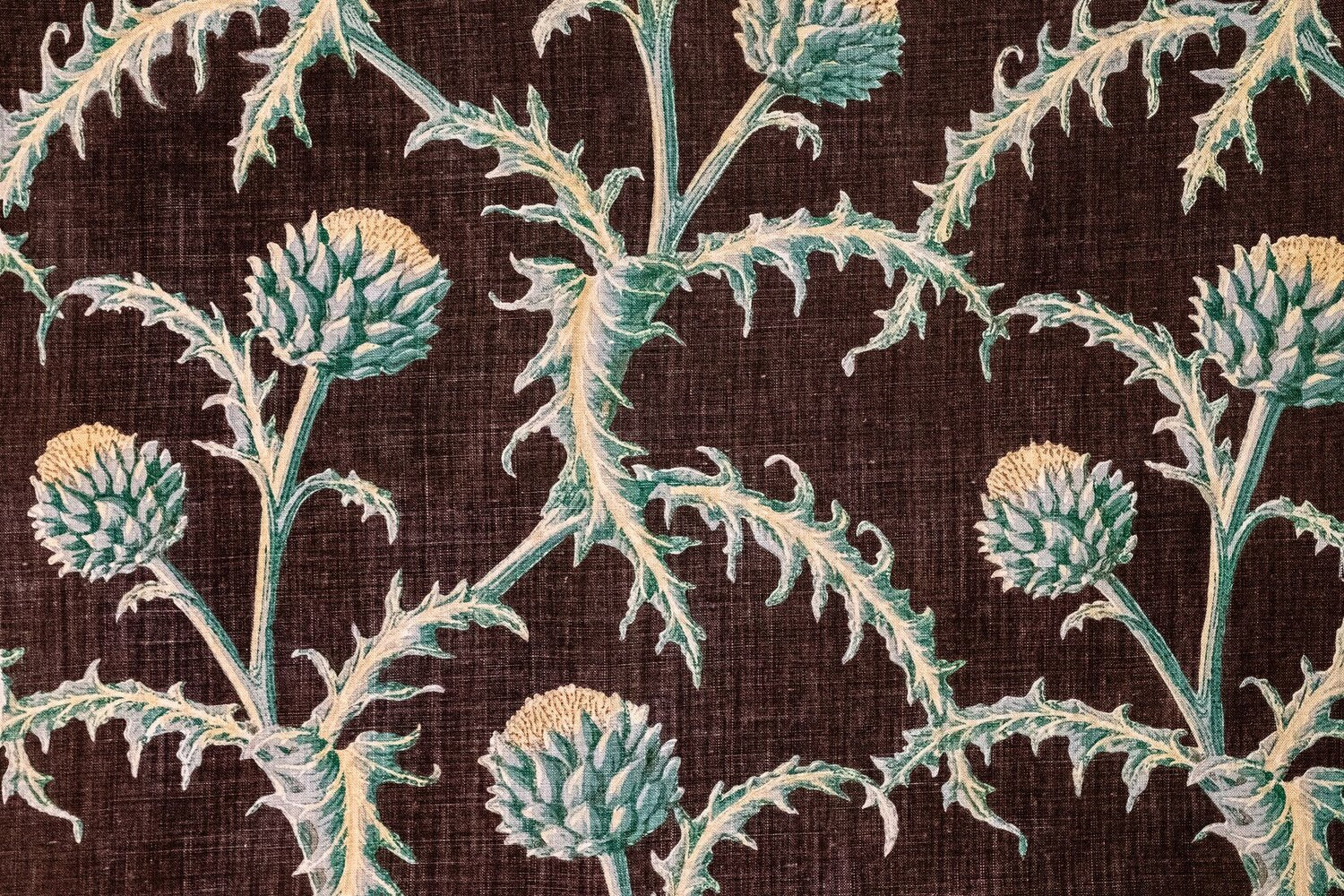 Detail of fabric in a repeating artichoke print in shades of turquoise and gold on a brown field.