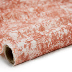 Partially unrolled fabric in an organic crumpled texture in coral on a cream field.