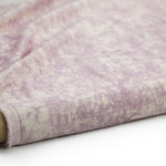 Partially unrolled fabric in an organic crumpled texture in light purple on a cream field.