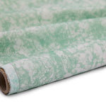 Partially unrolled fabric in an organic crumpled texture in light green on a cream field.