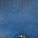 Two vases of flowers stand in front of a wall covered in an abstract ombré paint splatter print in blue, white and navy.