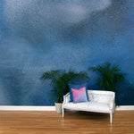 A sofa and potted plants stands in an abstract ombré paint splatter print in shades of blue, white and navy.