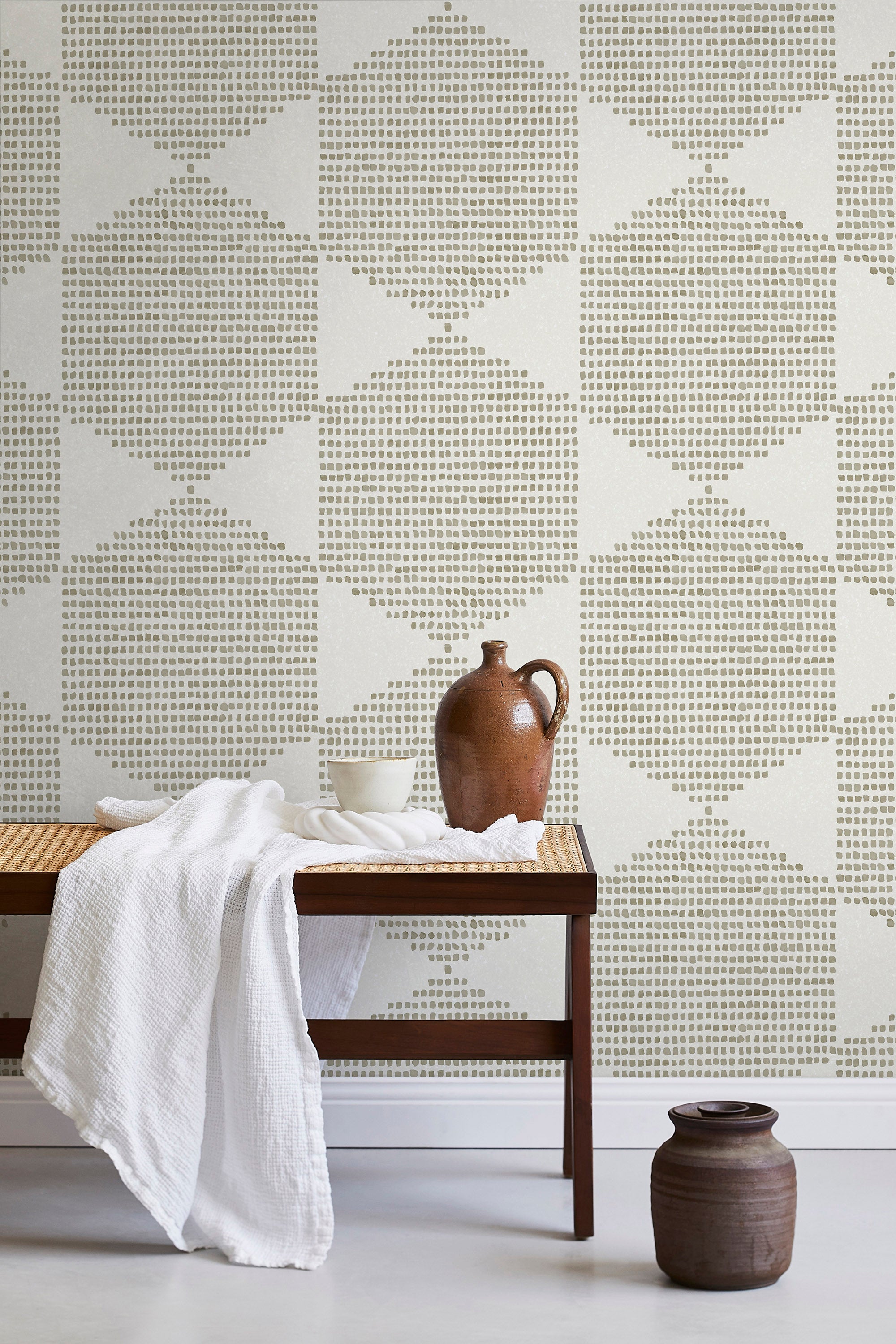 A bench with a towel and clay vases stands in front of a wall papered in a geometric star print in olive and cream.