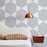 A modernist bed, hanging lamp and chair stand in front of a wall papered in a geometric star print in blue and cream.