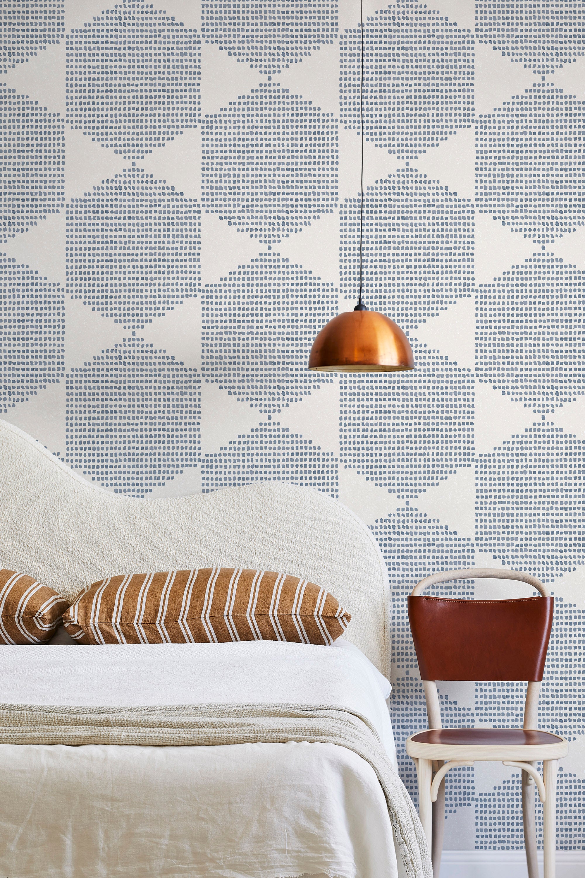 A modernist bed, hanging lamp and chair stand in front of a wall papered in a geometric star print in blue and cream.