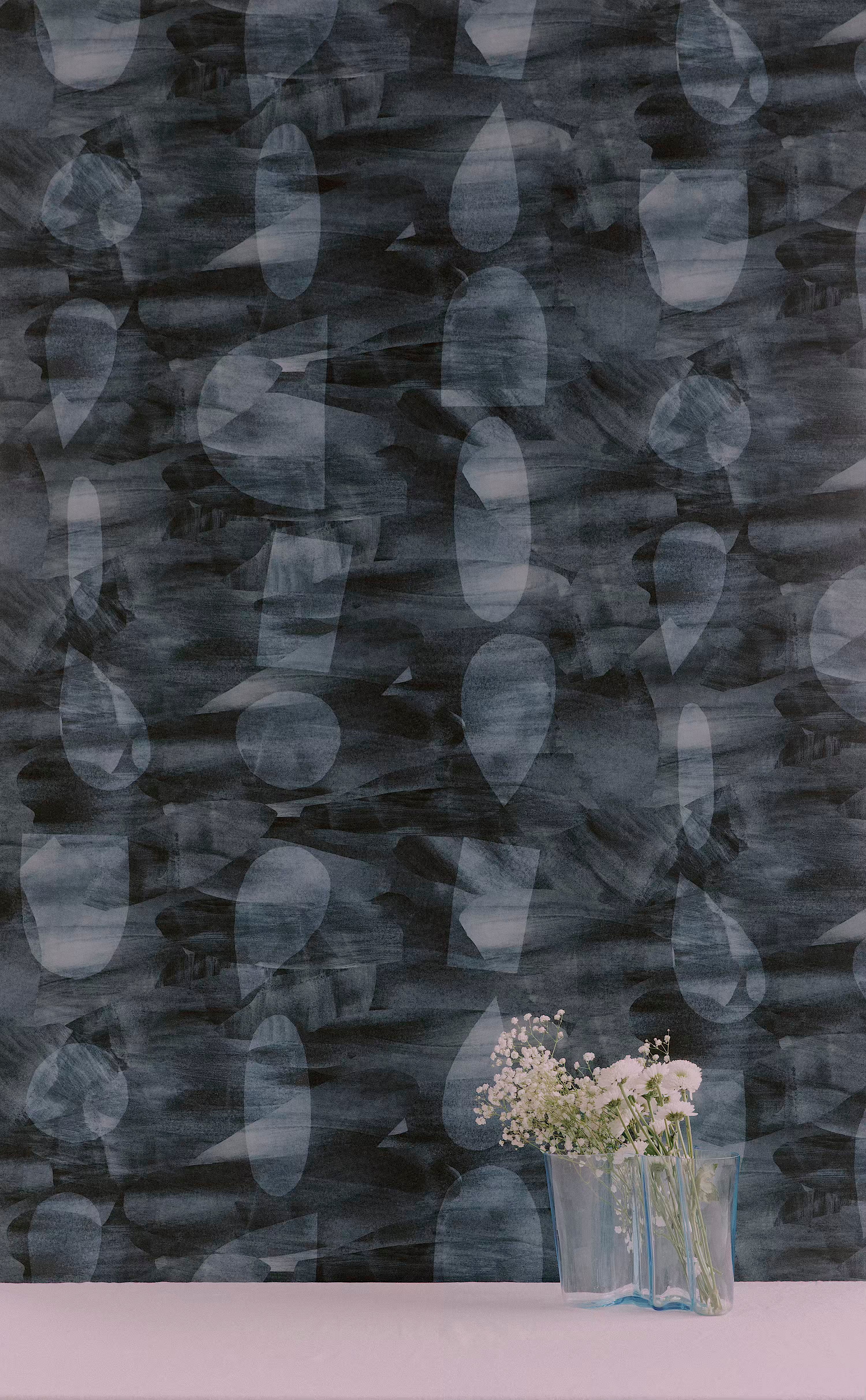 A vase of flowers stands in front of a wall papered in an abstract curvolinear pattern in blues, navy and black.