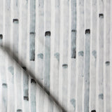 Detail of draped fabric in a painterly stripe print in gray on a white field.