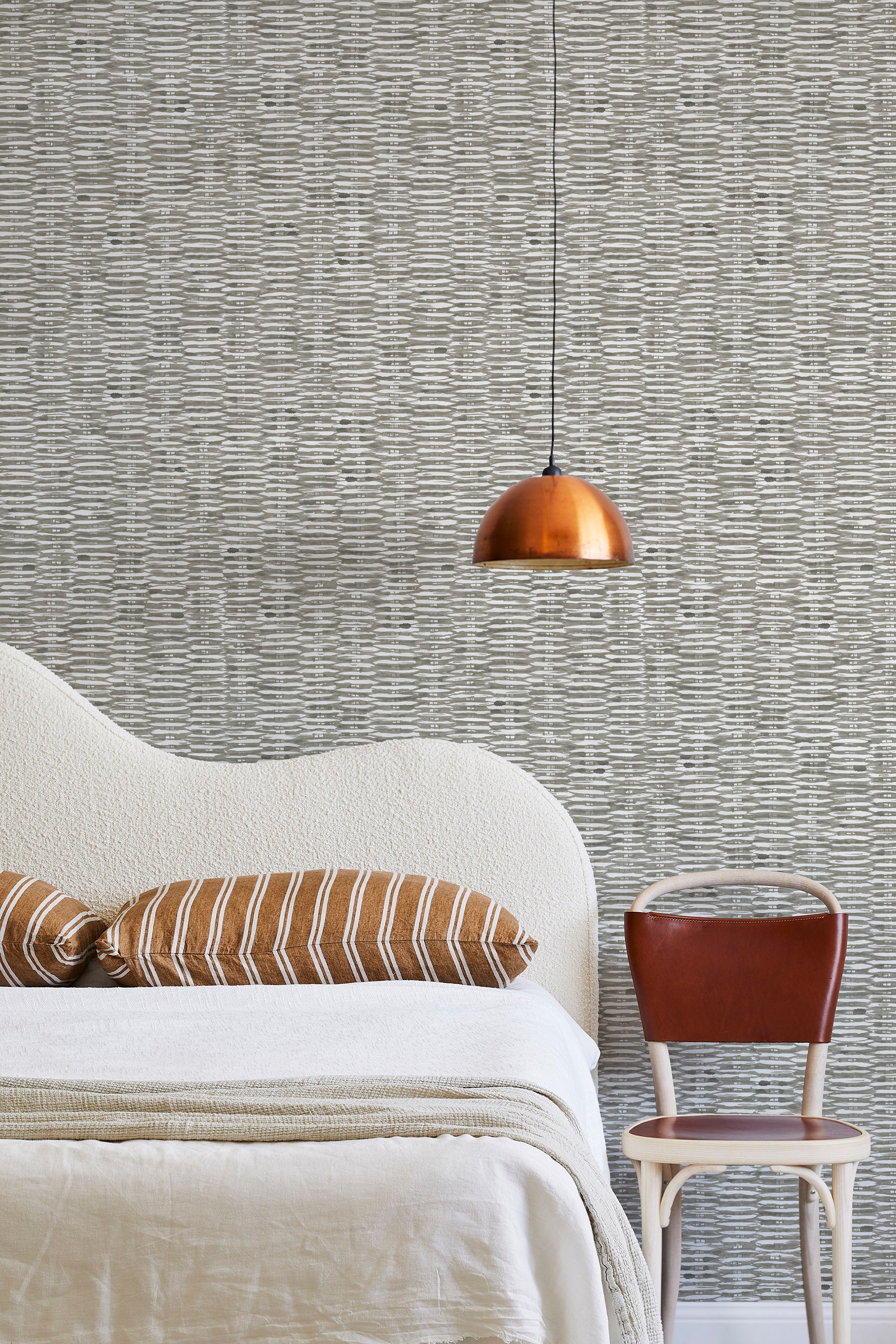 A modernist bed, hanging lamp and chair stand in front of a wall papered in a textural checked print in gray and white.