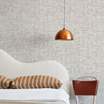 A modernist bed, hanging lamp and chair stand in front of a wall papered in a textural checked print in tan and white.