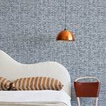 A modernist bed, hanging lamp and chair stand in front of a wall papered in a textural checked print in navy and white.