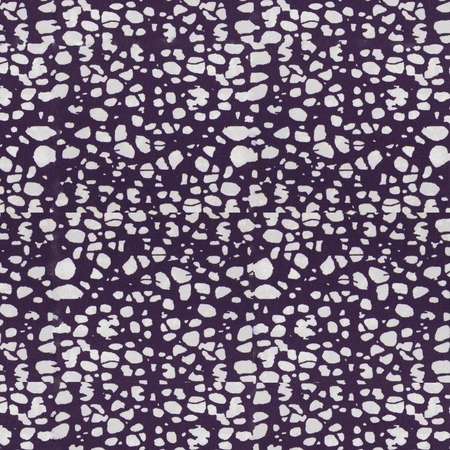 Detail of fabric in a batik splatter print in cream on a dark purple field.