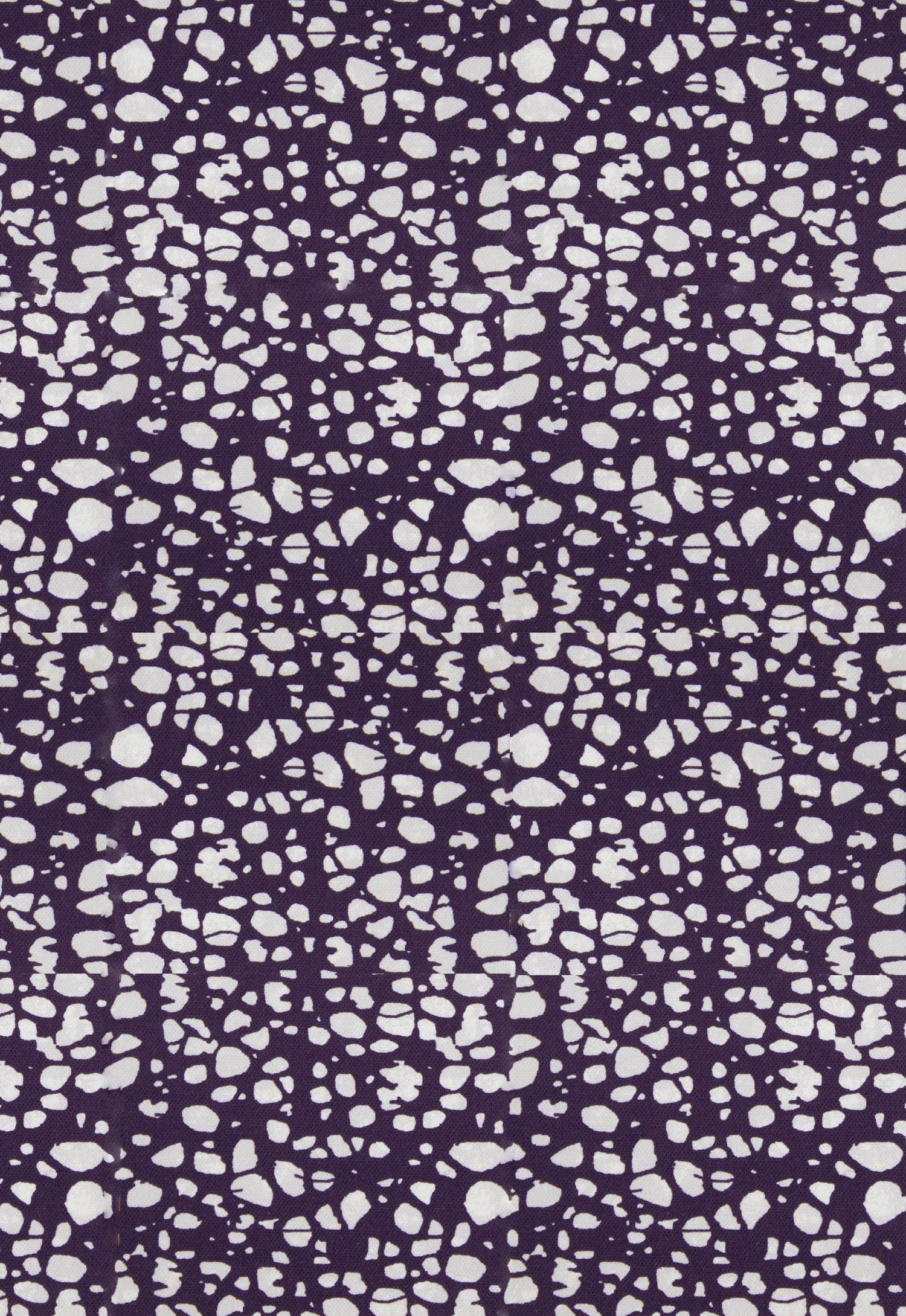 Detail of fabric in a batik splatter print in cream on a dark purple field.