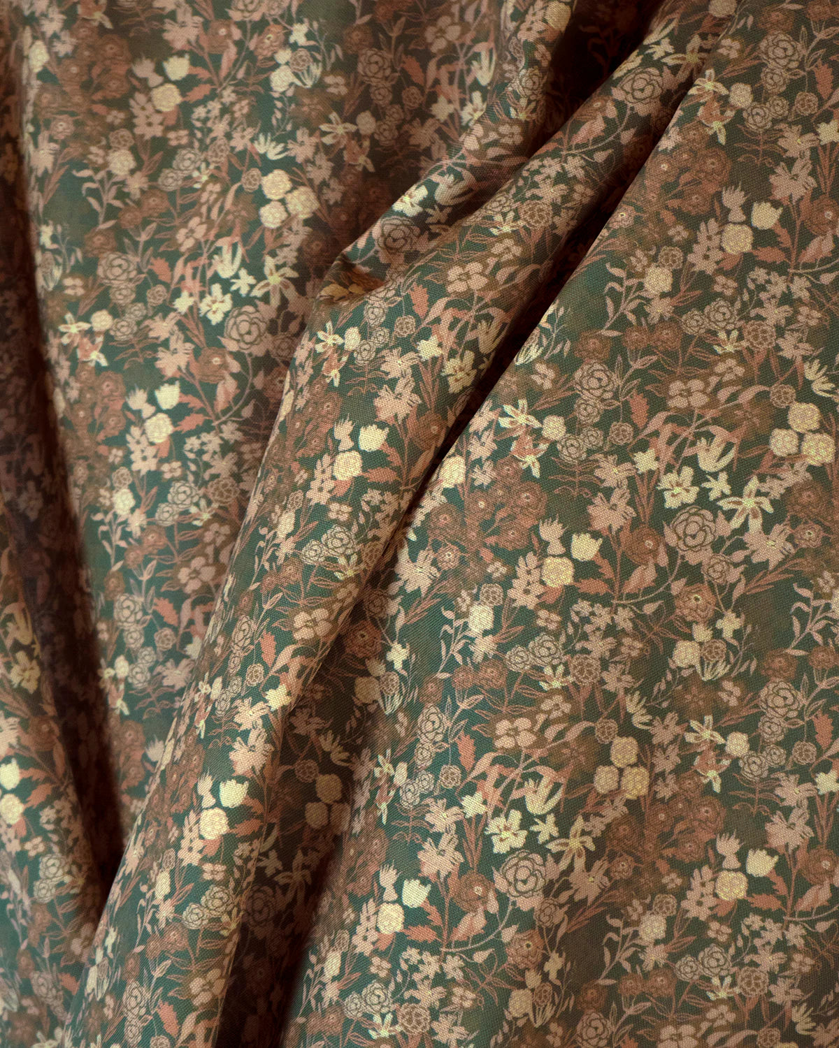 Draped fabric yardage in a dense small-scale floral print in shades of brown and tan on a green field.